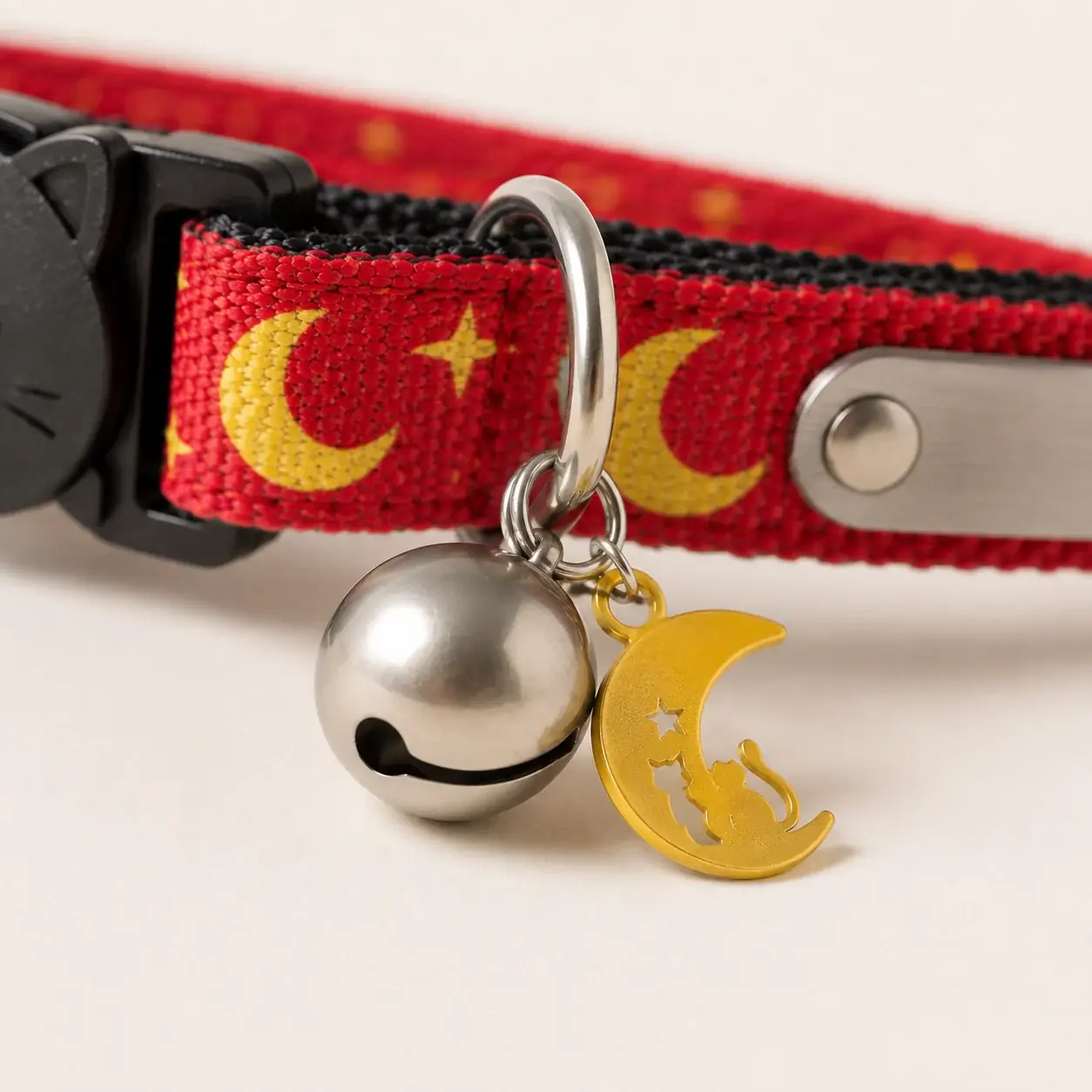 Close-up of the silver bell and the gold crescent moon charm hanging from the ring on a red strap