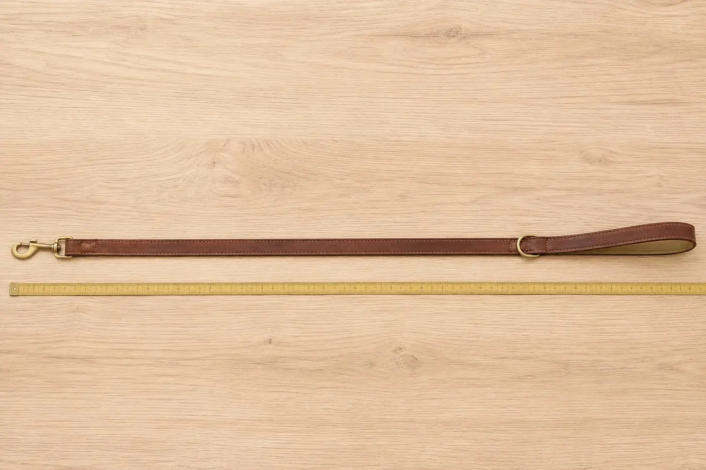 The brown leash laid out at full length on pale wood beside a measuring rule