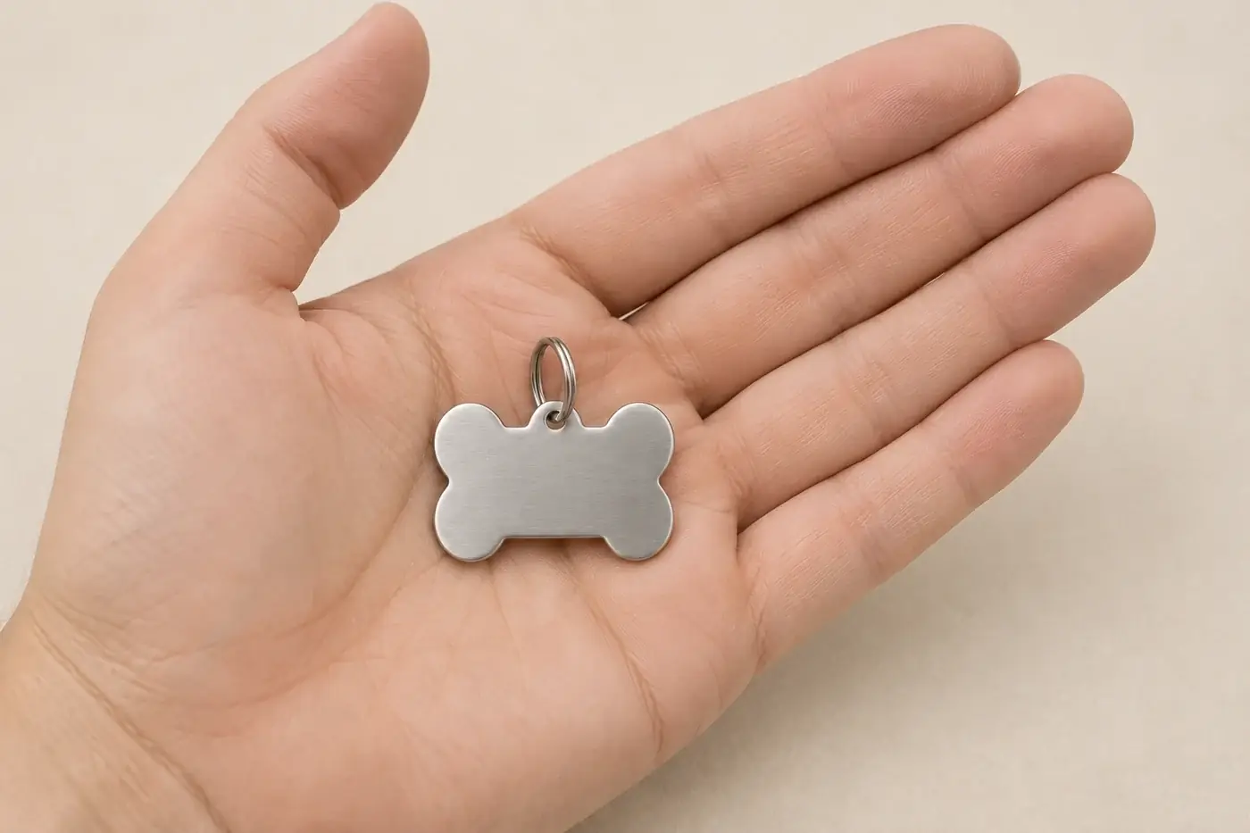A steel bone-shaped tag lying flat in an open palm, giving its scale against the fingers