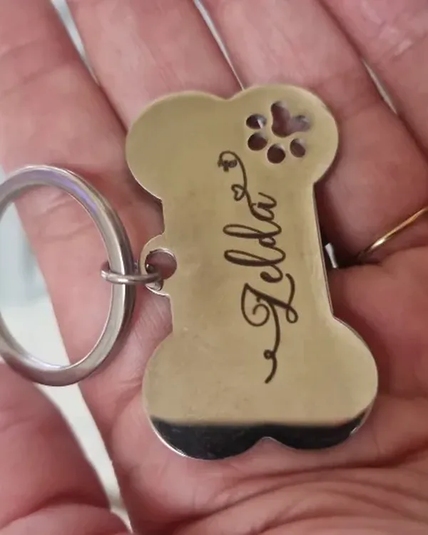Brass bone-shaped tag engraved "Zelda", held between two fingers