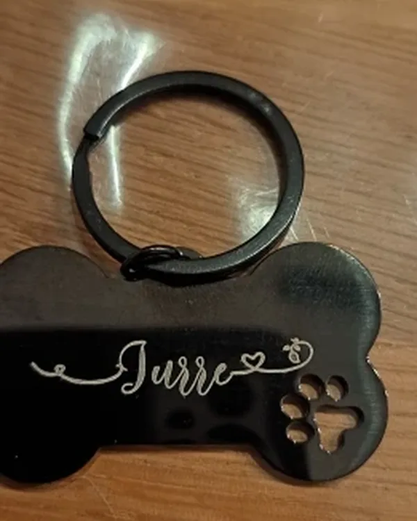 Black bone-shaped tag engraved "Jurre" on a black ring, resting on a wooden table