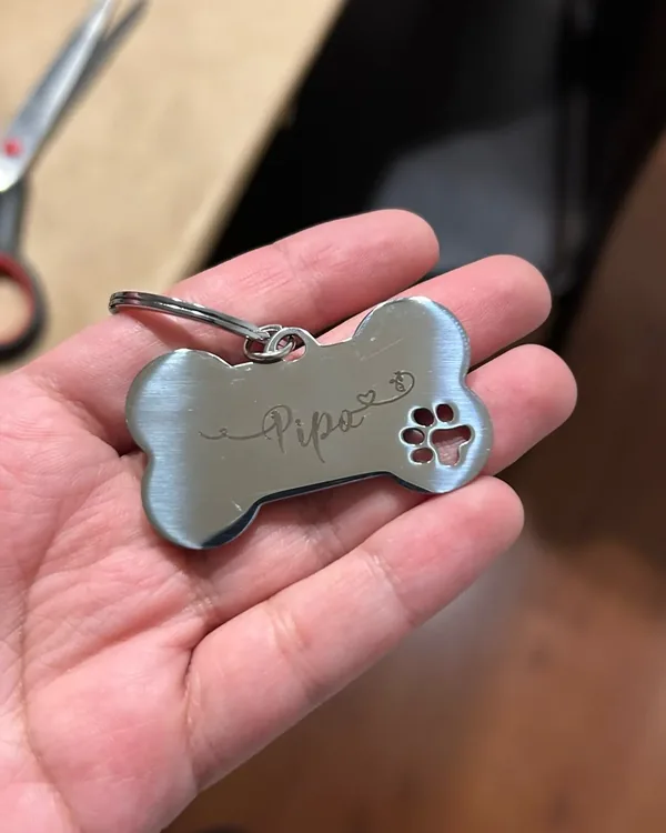 Steel bone-shaped tag engraved "Pipo" resting in an open palm